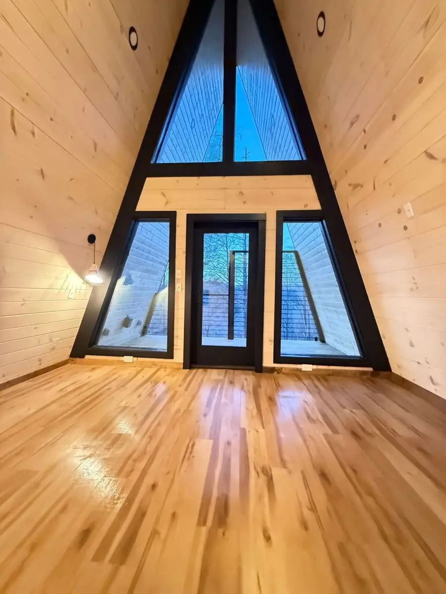 A-frame cabin loft with clean, shining hardwood floors and tall triangle windows at dusk