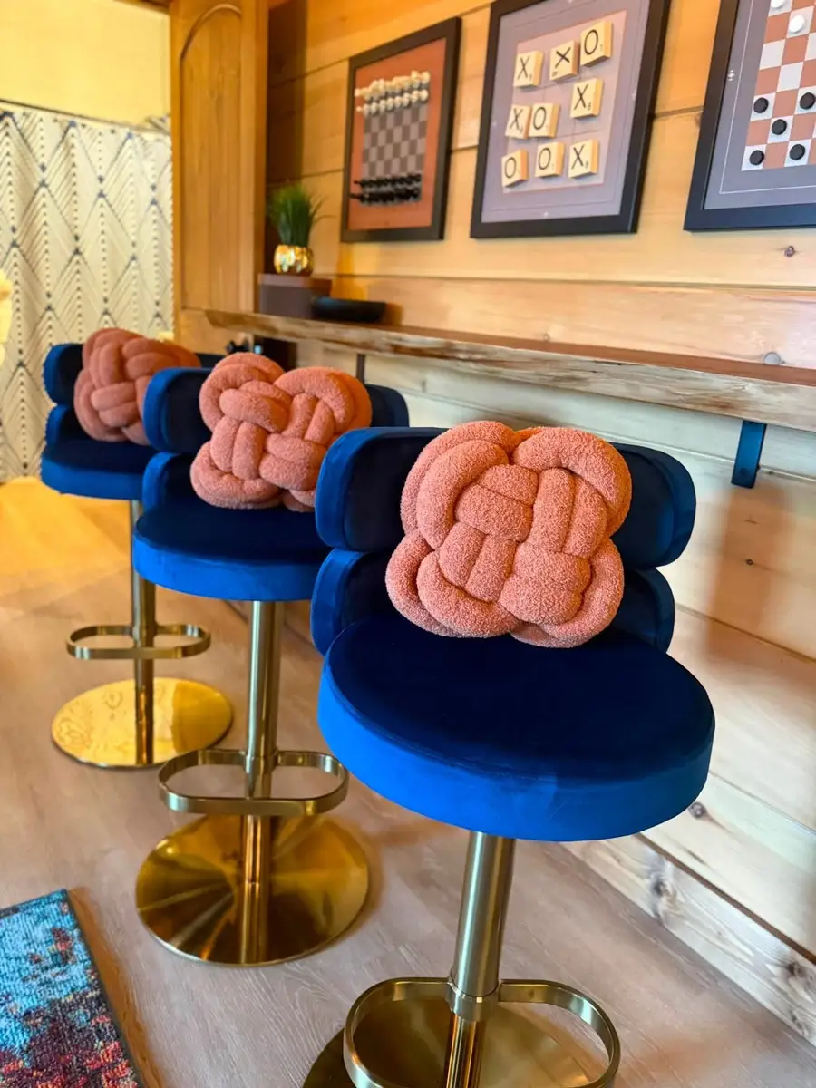 Blue velvet bar stools with knot pillows lined up at a wood bar in a cabin game room