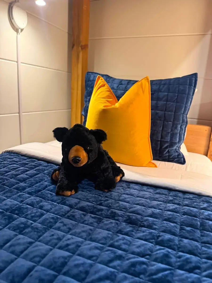 Navy quilted bed with a mustard pillow and a black bear plush placed for the next guests