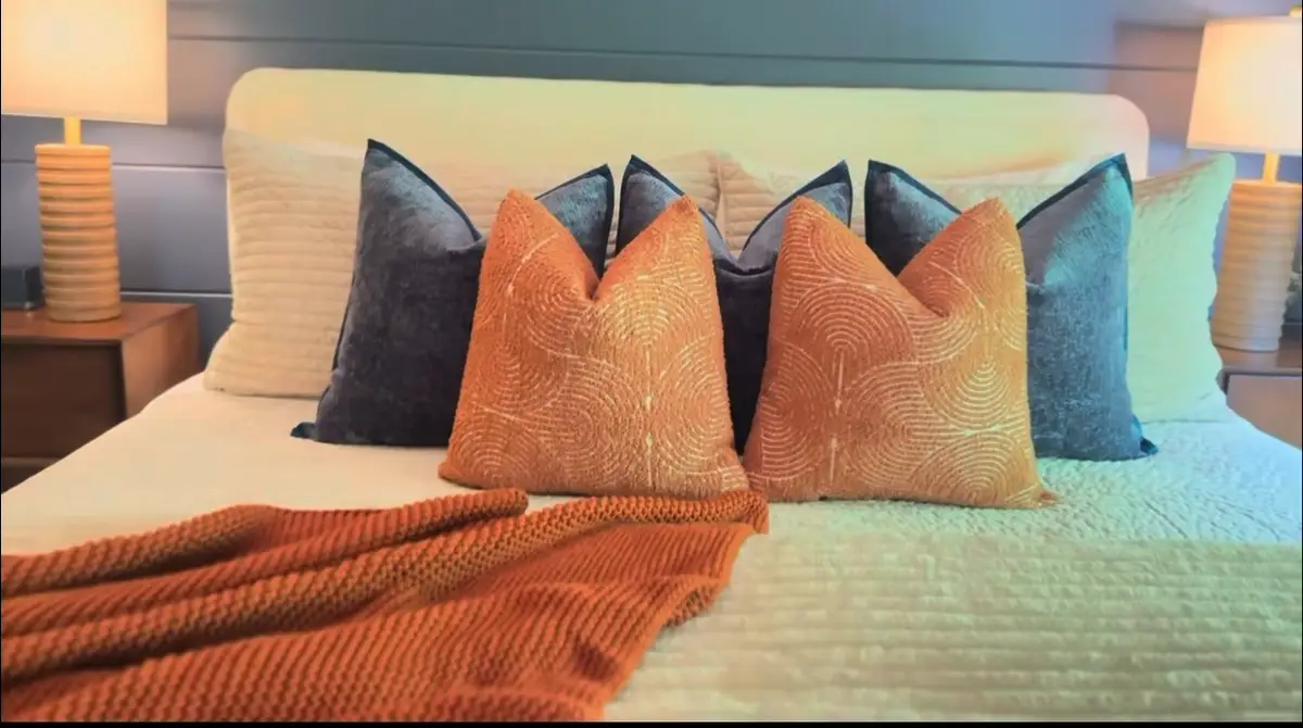 Made bed with orange and navy pillows and an orange throw