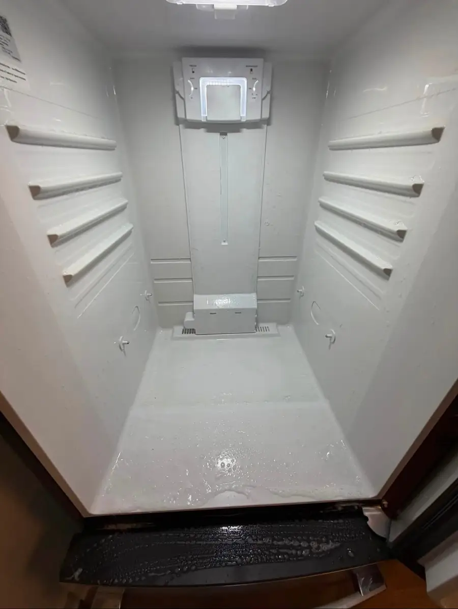 Inside of an emptied refrigerator being washed down, shelves and walls wet with soap