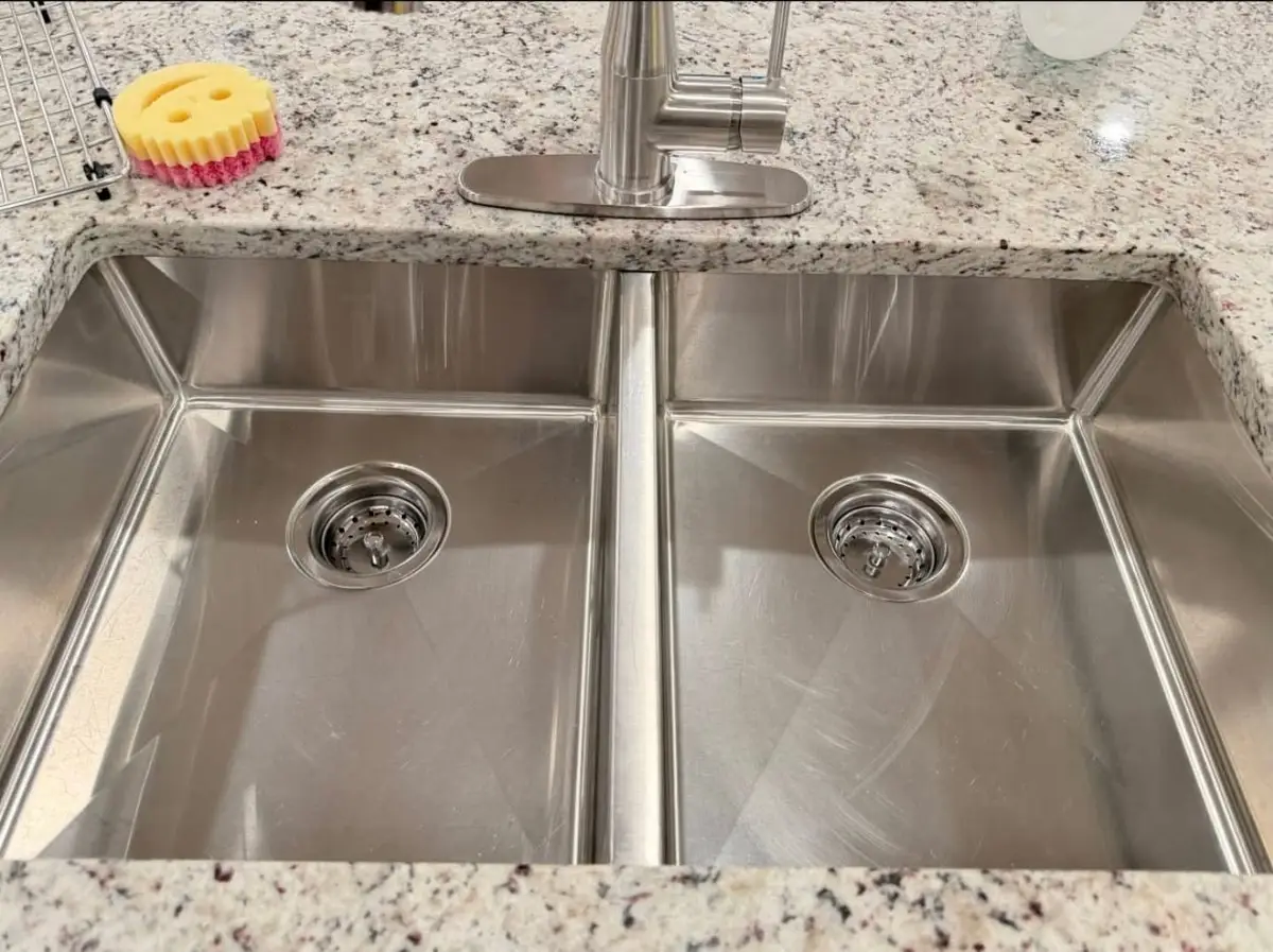 Double stainless steel kitchen sink scrubbed clean in a granite counter