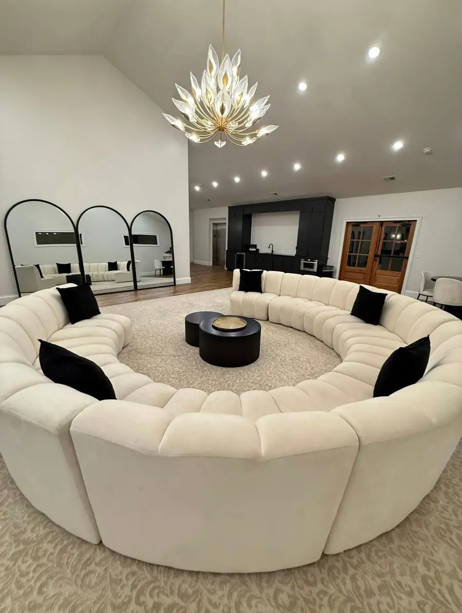Large lounge with a round white sofa, black pillows, arched mirrors and a crystal chandelier, cleaned and staged