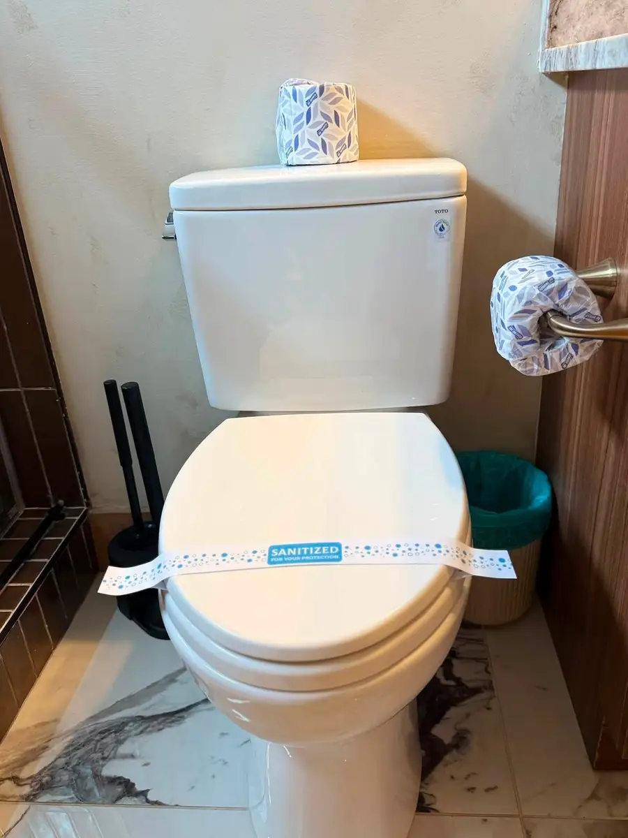 Toilet sealed with a "Sanitized for your protection" band and fresh wrapped paper rolls