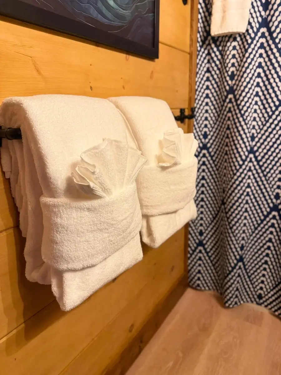 White towels folded hotel style on a black bar against a pine wall