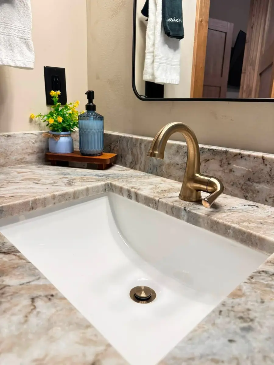 Granite bathroom vanity with a gold faucet, a blue soap bottle and a small yellow plant