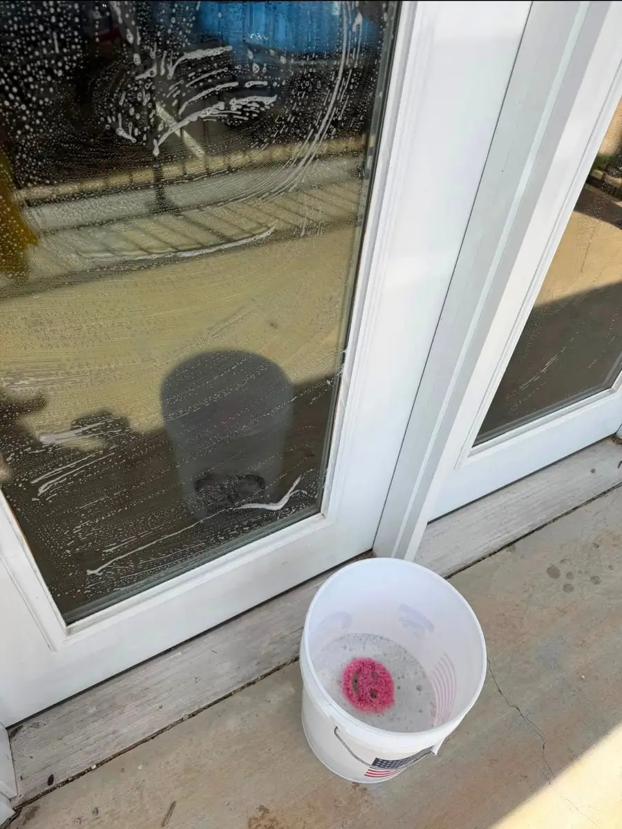 Glass patio door soaped up for washing, a bucket with a pink sponge at its foot